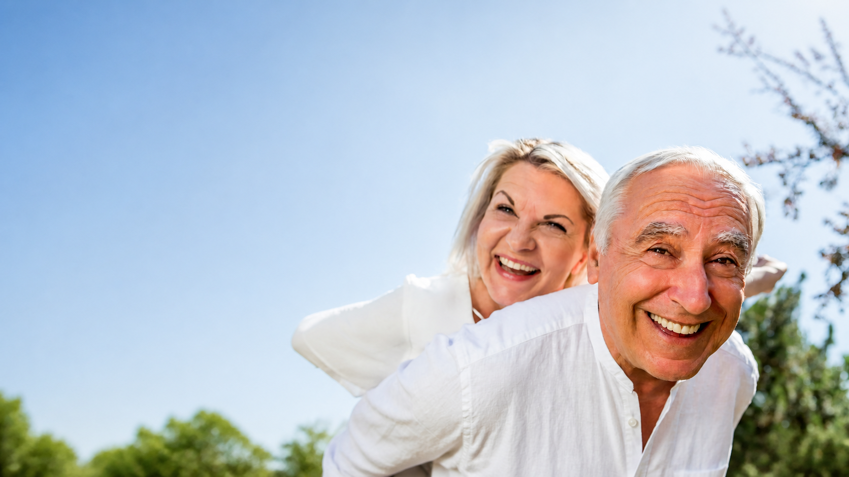 A happy older couple smiling together outdoors against a bright blue sky